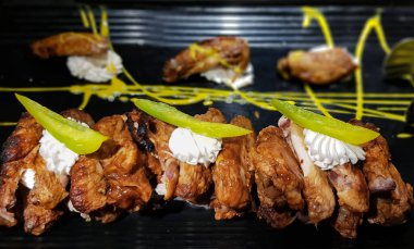 Baharatlı kızarmış tavuk parçaları ekşi krema sosuyla süslenmiş ve restoranda siyah bir tabakta servis edilmiş.