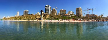 ISRAEL, NETanyA, MARCH, 2016 - Yeşil bir tepenin üzerinde yeni modern liman mimarisinin panoraması ve Netanya şehir plajında eğlenen insanlar, İsrail