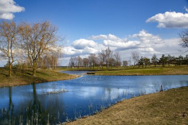 Riga, Letonya 'daki Kisezers kıyılarındaki su basmış çayırlar üzerindeki küçük göllerle güneşli bahar manzarası. Beyaz kümülüs bulutları suya yansıyor..