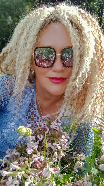 在拉脱维亚里加 一个戴着太阳镜 留着卷曲头发的漂亮女人躺在花草丛生的草地上 — 图库照片