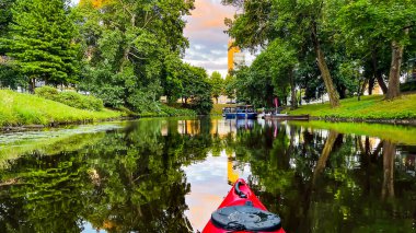 The red kayak floats along the city canal on sunset in downtown of Riga, the capital of Latvia.