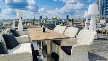 LATVIA, RIGA, AUGust, 2021 - Restoranın beyaz hasır mobilyalı açık verandası ve Riga Eski Kasabası 'nın çatıları, Letonya' nın başkenti