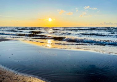 Letonya, Jurmala 'da Baltık Denizi üzerinde güzel turuncu gün batımı. Baltık Denizi 'nde akşam sakin olur. Sahilde gün batımında altın ıslak kum.