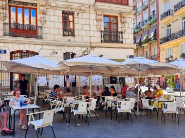 İspanya, VALENCIA, SEPTEMBER, 15, 2025: İnsanlar Valencia, İspanya 'da sıcak bir günde şemsiye altındaki bir restoranın açık verandasında hafif içecekler içip sohbet ediyorlar.