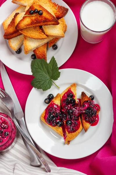 Lezzetli tost ekmeği ev yapımı frenk üzümü reçeli ve parlak kırmızı masa örtüsü üzerinde süt.