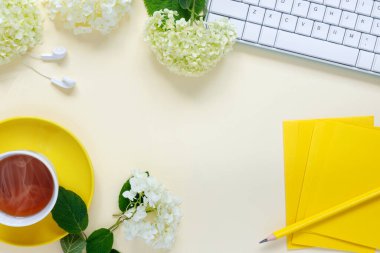 Top view of home office desk with laptop, cup of hot tea, and bouquet of hydrangeas  on yellow paper background.