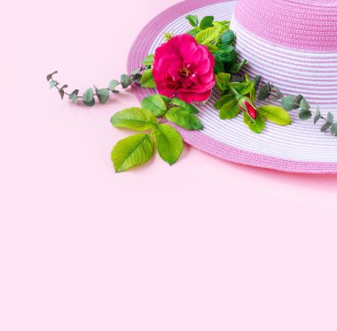 Güneşli bir günde gül buketi ve okaliptüslü güzel bir hasır şapka. Doğanın pembe kağıt arka planı.