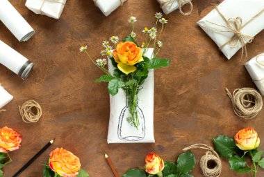 Altın arkaplanda el yapımı ambalaj kağıdı ve çiçekler. Ev yapımı vazo, sarı güller ve narin papatyalar ile ev yapımı el yapımı hediyeler..