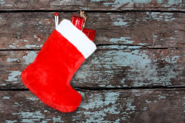 Arka plandaki tahta duvarda hediyeleri olan kırmızı Noel çizmesi.