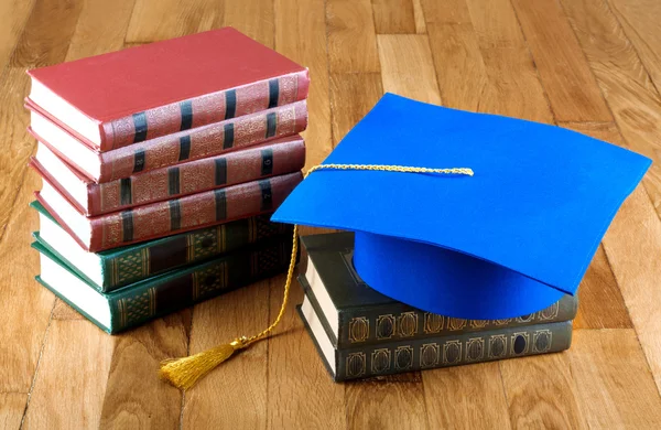 Avläggande av examen mortarboard på toppen av högen med böcker på trä bakgrunds — Stockfoto