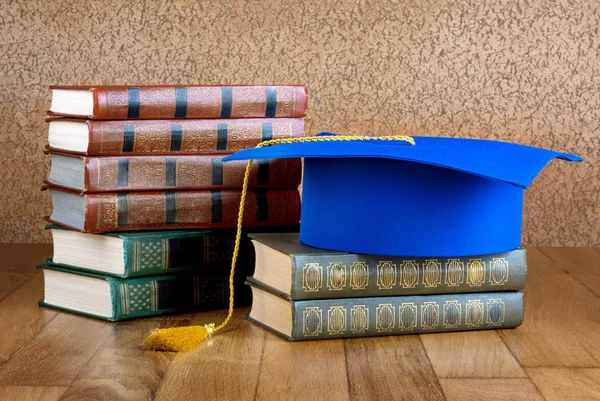 Mortero de graduación en la parte superior de la pila de libros en backgr de madera — Foto de Stock