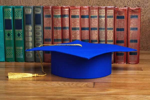 Afstuderen mortarboard boven op de stapel boeken op abstracte rug — Stockfoto