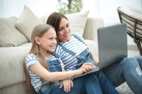 Mãe e filha sentado no tapete na sala de estar e usando um laptop — Fotografia de Stock