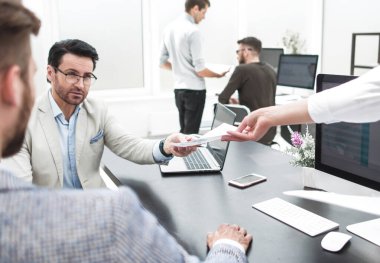 Sekreter ofisteki masaüstündeki iş adamına belgeleri veriyor.