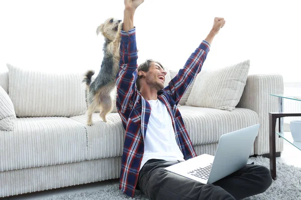 Cara feliz exulta com seu cão sentado perto do sofá na sala de estar. — Fotografia de Stock