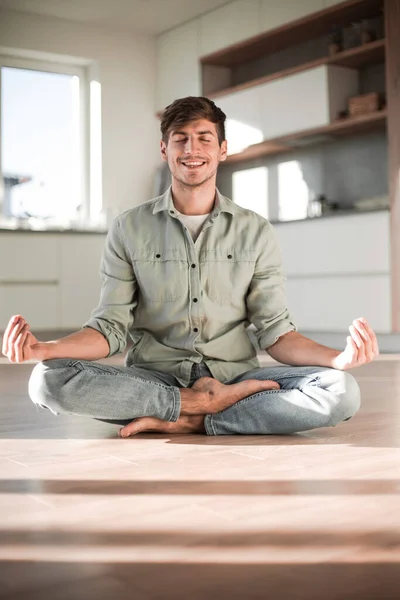 Jovem sentado na posição Lotus no chão da cozinha — Fotografia de Stock