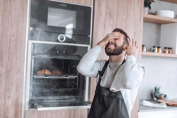 Surprised man standing near the oven with burnt croissants. — Stock Photo, Image