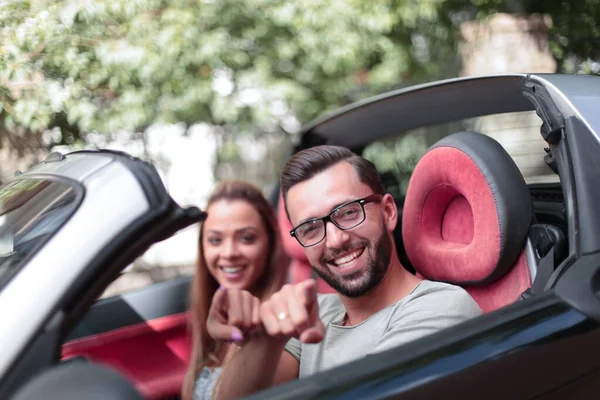 Feliz pareja sentado dentro de un convertible y apuntando a usted — Foto de Stock
