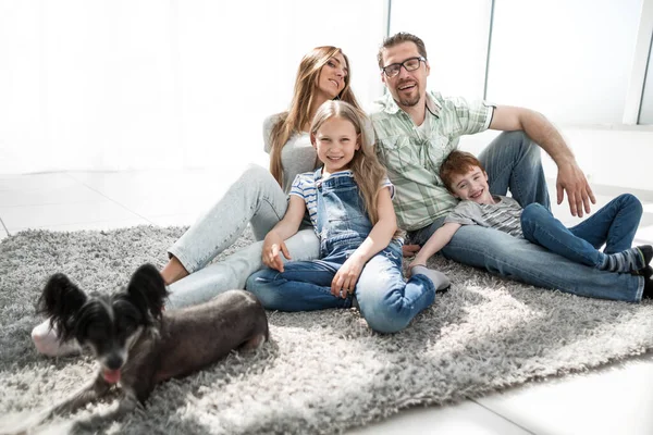 Šťastná rodina s domácím mazlíčkem sedí na koberci — Stock fotografie