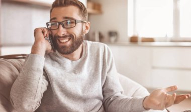 Rahat bir koltukta oturan neşeli bir adam cep telefonuyla konuşuyor.