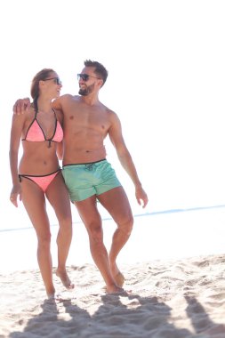 Genç çift el ele tutuşup kumsalda yürüyor..