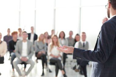 Kapat. Konuşmacı konferans odasında seyircilerin önünde duruyor.