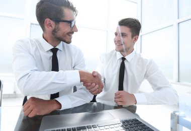 Başarılı genç iş ortakları kameraya gülümseyen bir masanın arkasında birlikte poz veriyorlar.