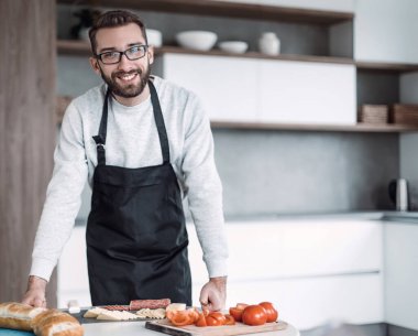 Önlüklü bir adam sandviçler için salam kesiyor.