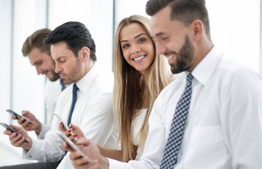 İş arkadaşları akıllı telefonları kullanıyorlar. Bekleme odasında oturuyorlar.