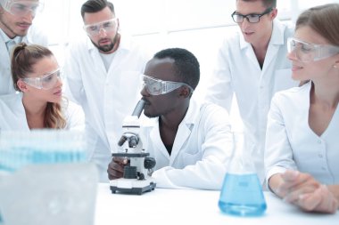 Odaklanmış ve ciddi kadın ve erkek kimyagerler laboratuvar önlükleri ve güvenlik gözlükleri takıp deneyler yapıyorlar.