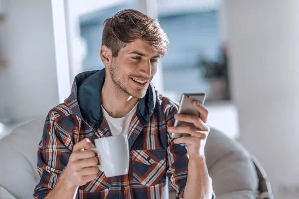 Atrakcyjny młody człowiek pije kawę i czyta SMS. — Zdjęcie stockowe