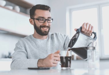 Çekici adam kendine bir fincan sabah kahvesi dolduruyor.