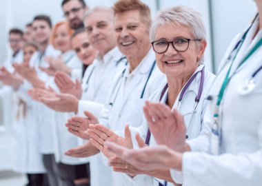 Gülümseyen bayan doktor alkışlayan meslektaşlarının önünde duruyor..