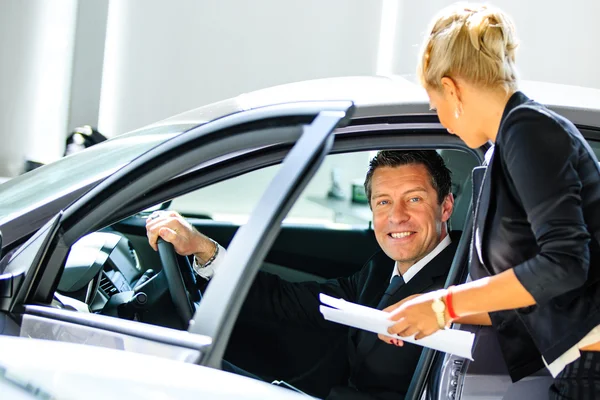 Jonge man kiezen voor auto op salon met hulp van consultant — Stockfoto