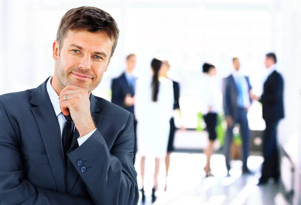 Portret van jonge knappe zakenman in kantoor met collega's op de achtergrond — Stockfoto