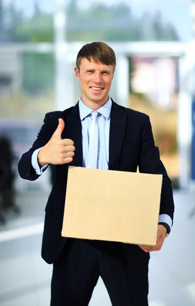 Smiling businessman holding a cardboard box and standing into an — Stock Photo, Image