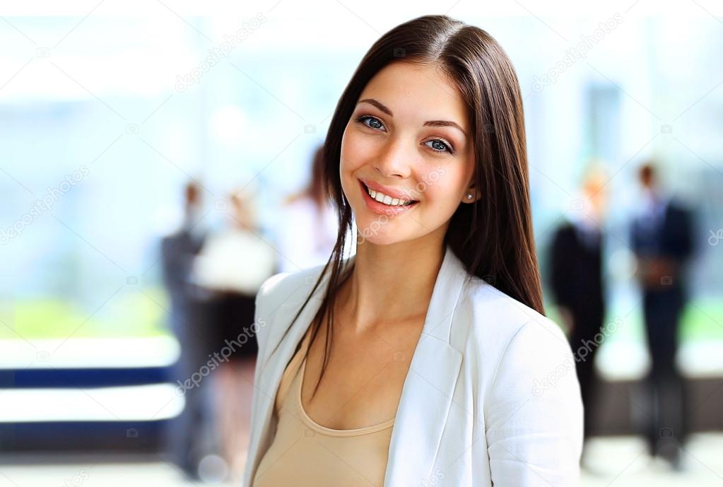 Smiling confident business woman looking at camera with her colleagues in background at office