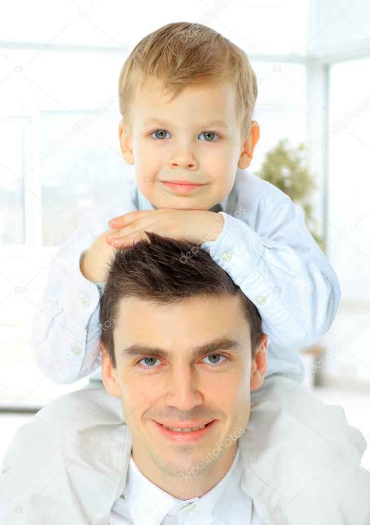portrait of the father  holding his son on his shoulders. both look at the camera and smiling