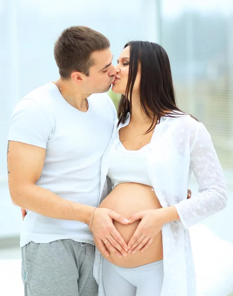 Hombre besando a su esposa embarazada. sus manos ilustran el corazón en su protuberancia del bebé — Foto de Stock