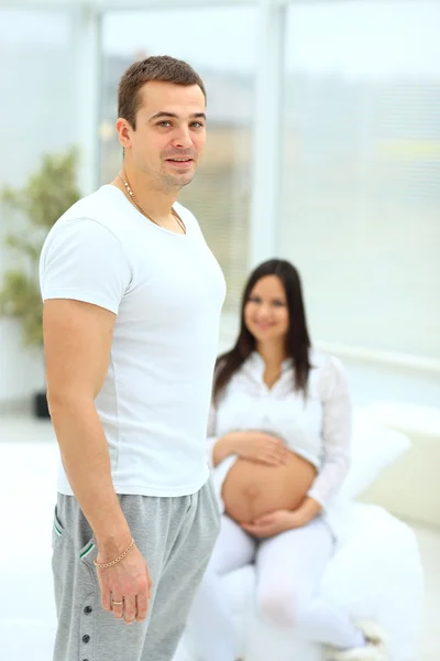 Ein Mann steht im Schlafzimmer, im Hintergrund sitzt seine schwangere Frau — Stockfoto