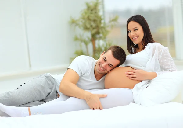 Der Mann lehnte sich an den Babybauch seiner schwangeren Frau, die auf dem Bett liegt — Stockfoto