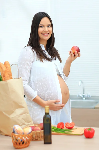 Gravid kvinna äta äpplet på bakgrunden av ett paket med produkter — Stockfoto