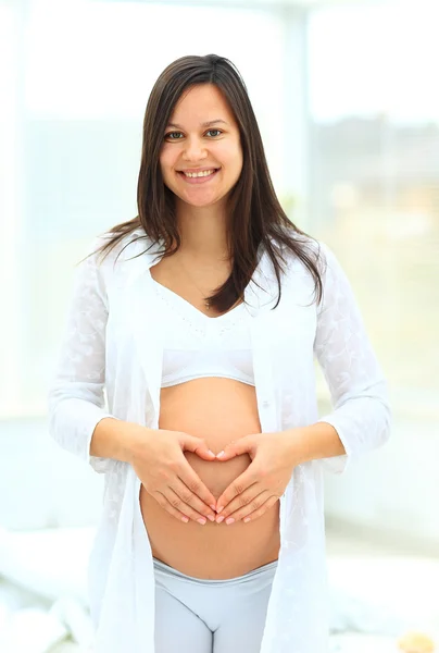 Gravid kvinna visar hjärtat på sin baby bump av händer — Stockfoto