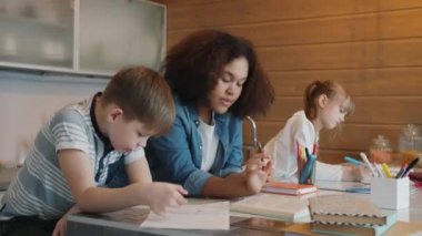 Afrikalı Amerikalı dadı eğitmeni çalışkan çocuklara ev ödevlerinde yardım ediyor.