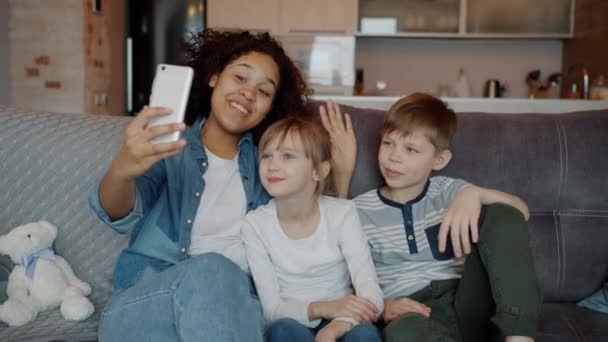 Câmera lenta de babá e crianças menino e menina fazendo chamada de vídeo on-line falando olhando para a tela do smartphone — Vídeo de Stock