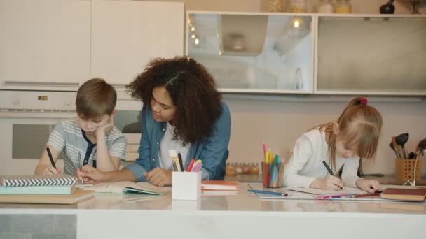Serious kids boy and girl doing homework with caring babysitter at home — Stock Video