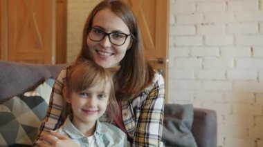 Mutlu genç aile portresi. Anne ve küçük kız gülümsüyor. Kapalı alanda kameraya bakıyor.