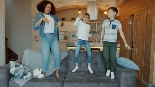 Lambat gerak anak-anak bahagia melompat di sofa dengan babysitter menari musik bersenang-senang — Stok Video
