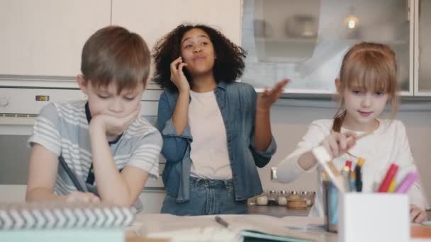 Porträt intelligenter Kinder beim Hausaufgabenschreiben, während sorglose Kindermädchen auf dem Handy chatten — Stockvideo