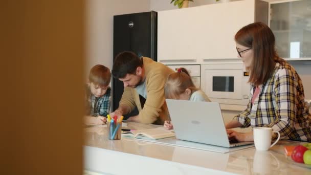 Movimento lento de jovens pais felizes da família e crianças estudando fazendo lição de casa na cozinha — Vídeo de Stock